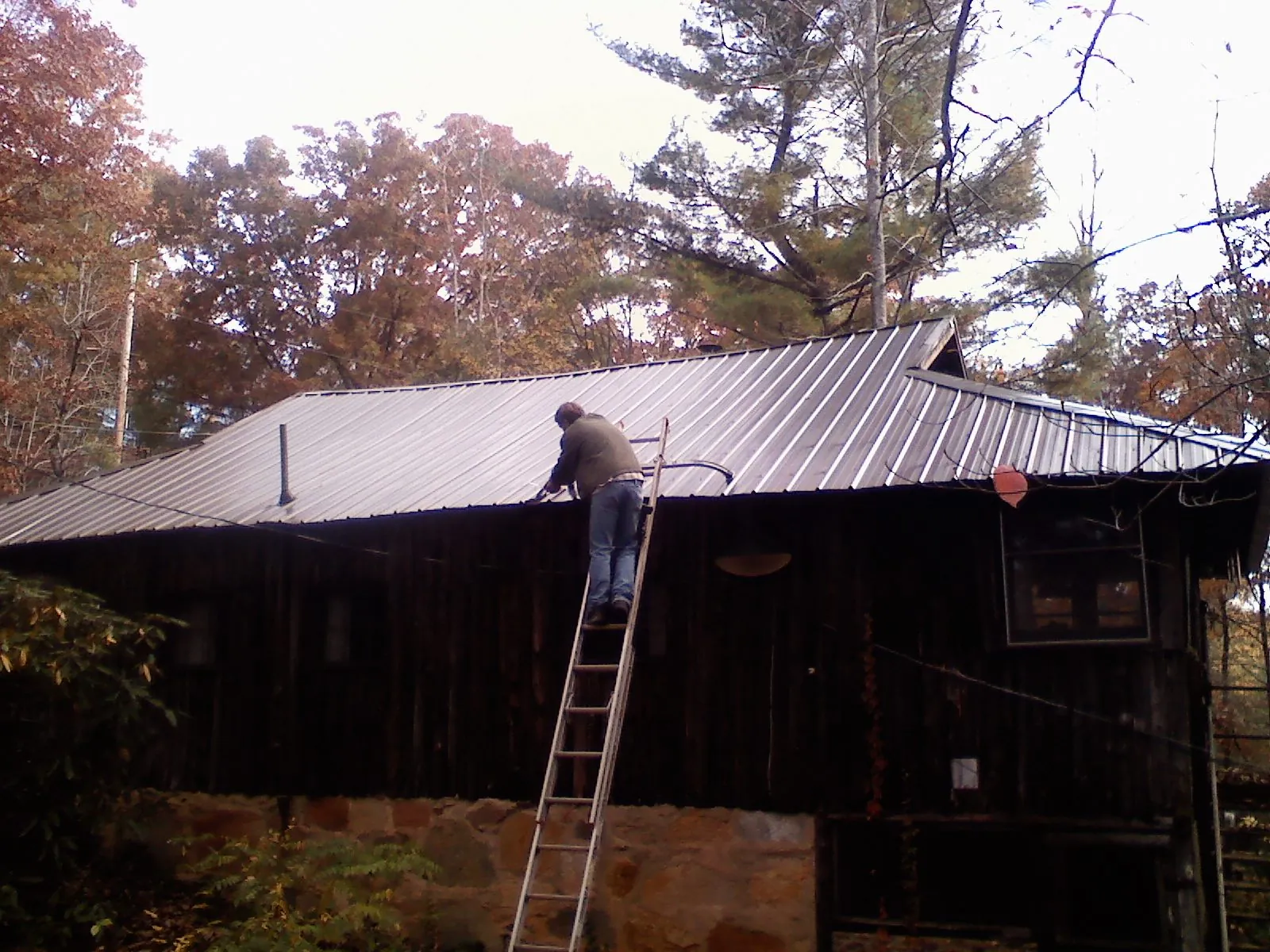 Roofer on a ladder working along the edge of a cabin metal roof in Utica