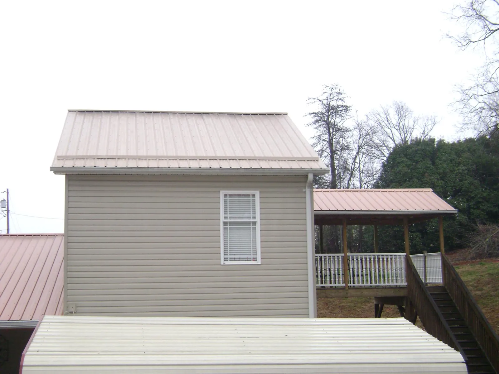 Tan metal roofs on a two story addition and attached porch, from a Roof Replacement job in Utica